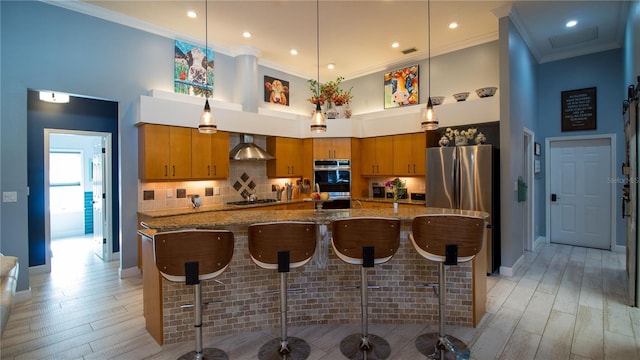 kitchen featuring hanging light fixtures, hardwood / wood-style flooring, stainless steel appliances, crown molding, and wall chimney range hood