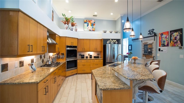 kitchen with a kitchen bar, sink, crown molding, appliances with stainless steel finishes, and wall chimney range hood