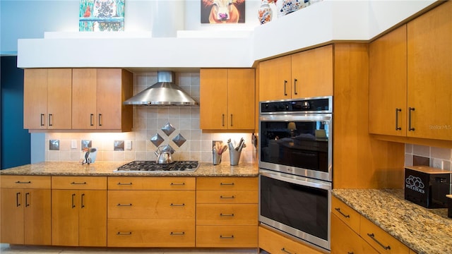 kitchen featuring stainless steel appliances, tasteful backsplash, light stone counters, and wall chimney exhaust hood