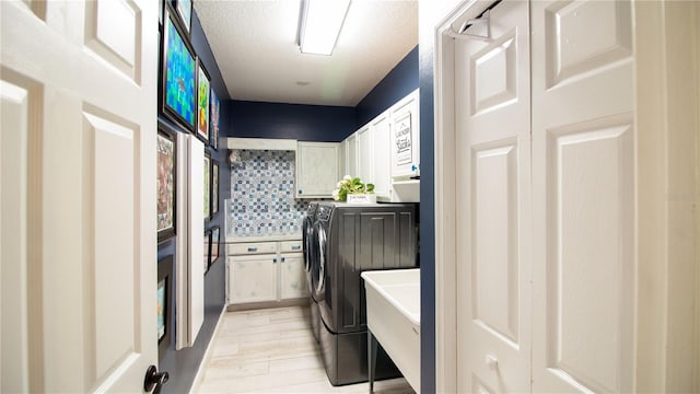 washroom with washing machine and clothes dryer, sink, cabinets, light hardwood / wood-style flooring, and a textured ceiling