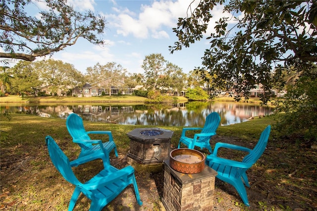 view of community featuring a water view, a lawn, and an outdoor fire pit