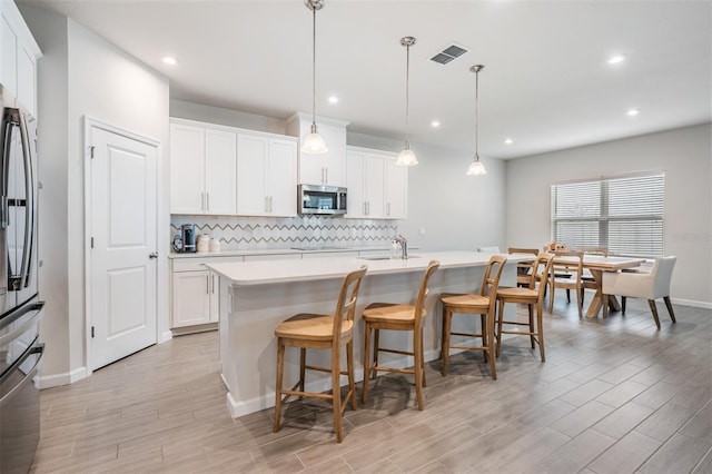 kitchen with pendant lighting, white cabinets, decorative backsplash, a kitchen island with sink, and stainless steel appliances