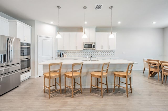 kitchen with white cabinetry, tasteful backsplash, hanging light fixtures, appliances with stainless steel finishes, and an island with sink