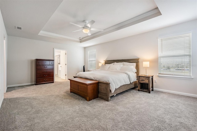 bedroom featuring light carpet, a tray ceiling, ensuite bath, and ceiling fan