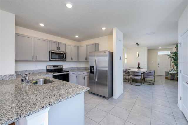 kitchen with kitchen peninsula, sink, light tile patterned floors, light stone counters, and stainless steel appliances