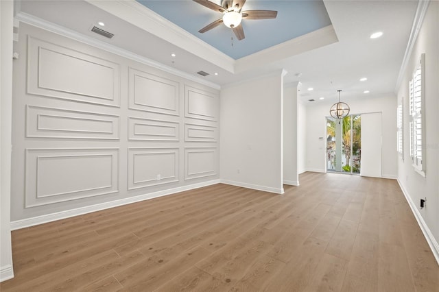 unfurnished living room with a raised ceiling, ceiling fan, ornamental molding, and light hardwood / wood-style flooring