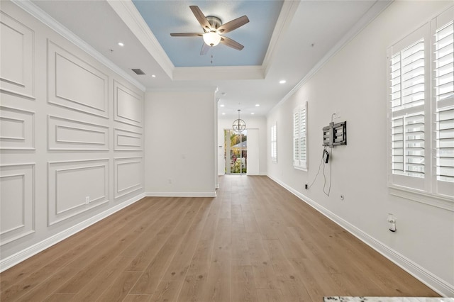 interior space with ceiling fan, ornamental molding, a raised ceiling, and light wood-type flooring