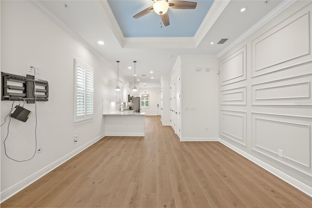 interior space with a raised ceiling, light wood-type flooring, crown molding, and ceiling fan