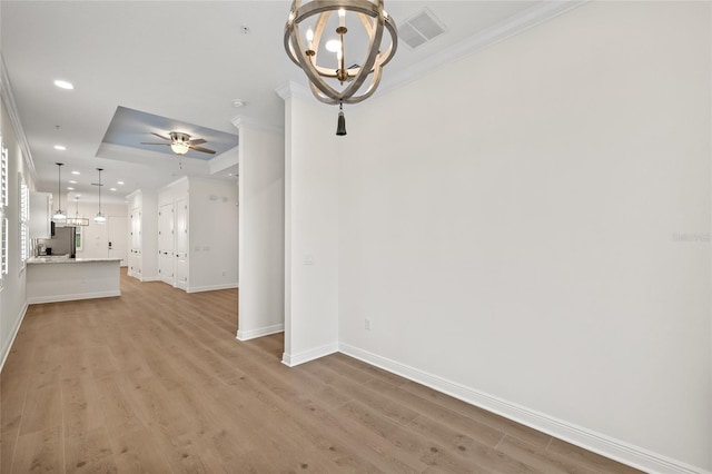 interior space with crown molding, ceiling fan with notable chandelier, a tray ceiling, and light hardwood / wood-style flooring