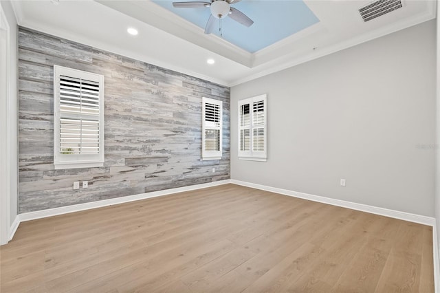 spare room with ceiling fan, wood walls, light hardwood / wood-style floors, a raised ceiling, and ornamental molding