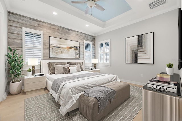 bedroom with wood walls, a raised ceiling, ceiling fan, light hardwood / wood-style flooring, and crown molding