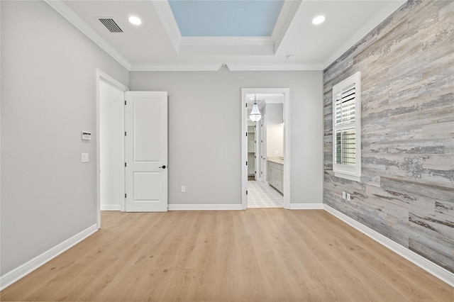 unfurnished bedroom featuring ornamental molding, light hardwood / wood-style floors, connected bathroom, and a raised ceiling