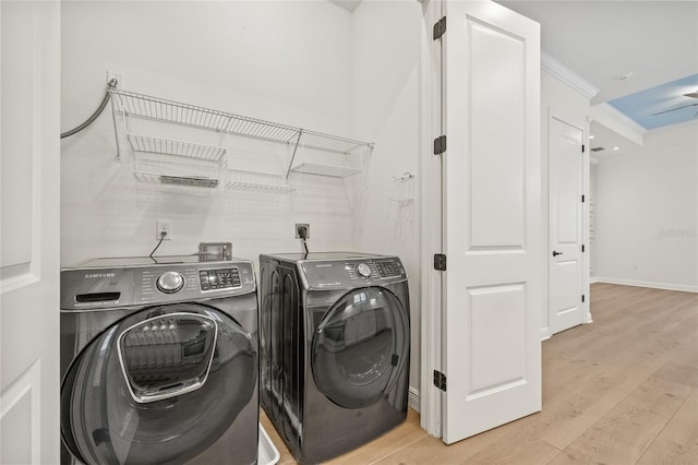 clothes washing area featuring light wood-type flooring, ornamental molding, and washing machine and clothes dryer