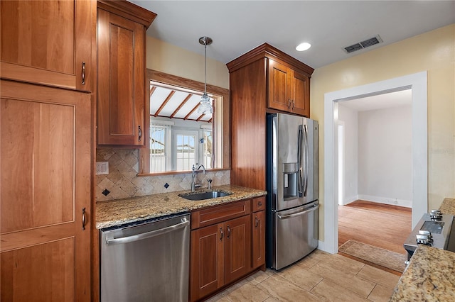 kitchen with sink, appliances with stainless steel finishes, light stone counters, tasteful backsplash, and decorative light fixtures