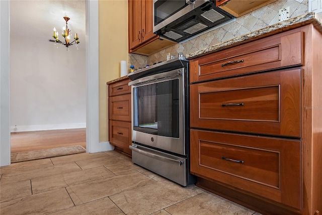 kitchen featuring light stone counters, decorative backsplash, stainless steel appliances, and an inviting chandelier