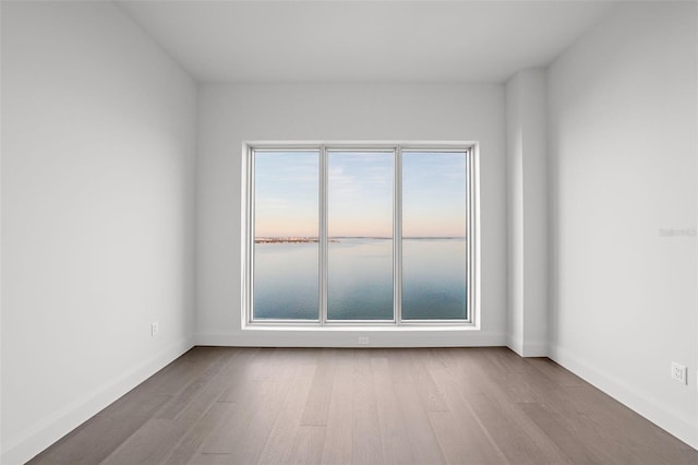 empty room with a water view, baseboards, and wood finished floors