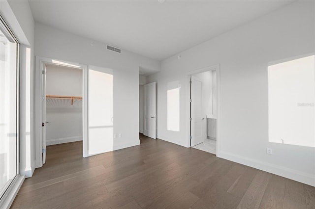 unfurnished bedroom featuring ensuite bathroom, wood finished floors, visible vents, a spacious closet, and a closet