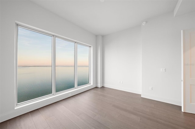 empty room featuring dark wood-type flooring, a water view, and baseboards