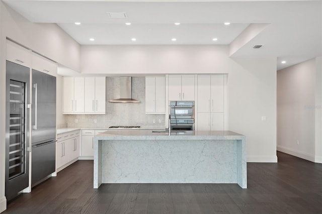 kitchen with visible vents, appliances with stainless steel finishes, backsplash, wall chimney exhaust hood, and a center island with sink