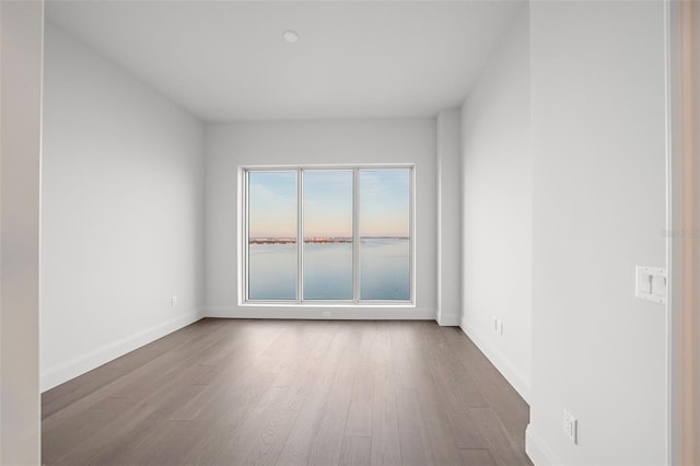 empty room with a water view, wood finished floors, and baseboards