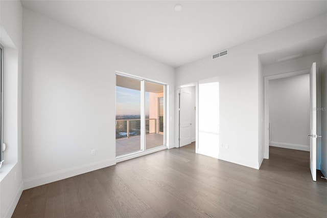 empty room with wood finished floors, visible vents, and baseboards