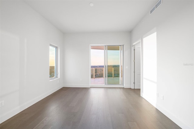 empty room featuring dark wood-style floors, visible vents, and a healthy amount of sunlight