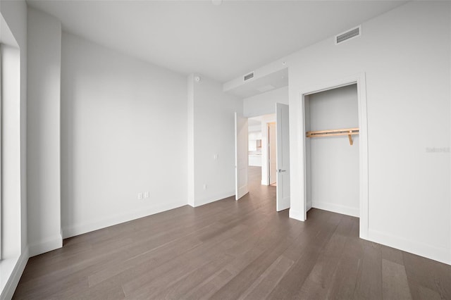 unfurnished bedroom with dark wood-type flooring, a closet, visible vents, and baseboards