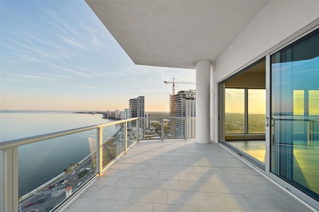 balcony at dusk with a water view and a view of city