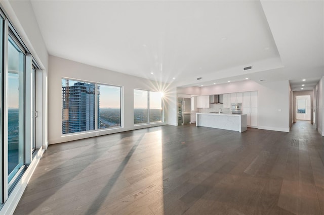 unfurnished living room with dark wood-style flooring, recessed lighting, baseboards, and a sink