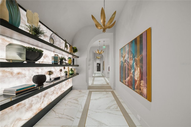 hallway with marble tiled floors, baseboards, arched walkways, a chandelier, and vaulted ceiling