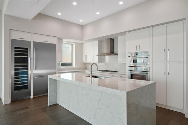 kitchen with wall chimney range hood, stainless steel appliances, a sink, modern cabinets, and dark wood-type flooring