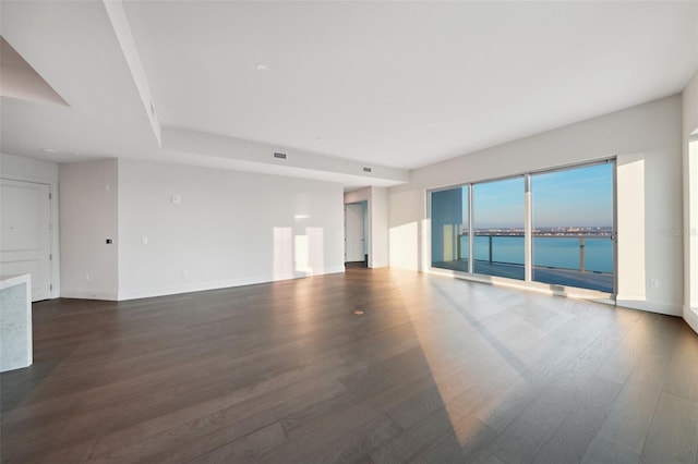 unfurnished living room with dark wood-style flooring, a water view, and baseboards