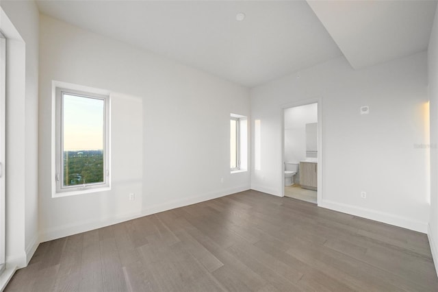 unfurnished bedroom featuring wood finished floors, ensuite bath, and baseboards