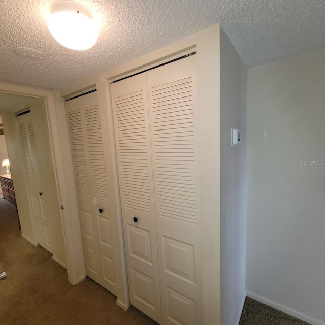 hall with dark carpet and a textured ceiling