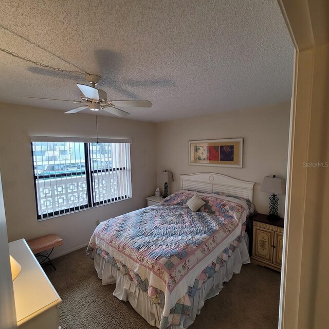 bedroom featuring ceiling fan, dark carpet, and a textured ceiling