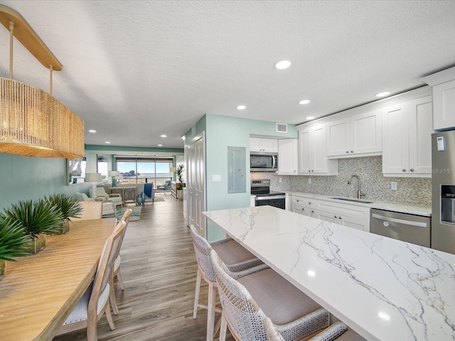 kitchen featuring sink, white cabinetry, hanging light fixtures, light stone countertops, and stainless steel appliances