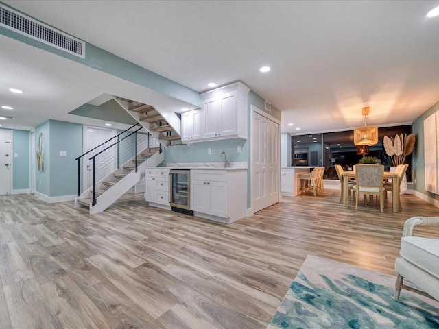 kitchen featuring wine cooler, pendant lighting, sink, light wood-type flooring, and white cabinets