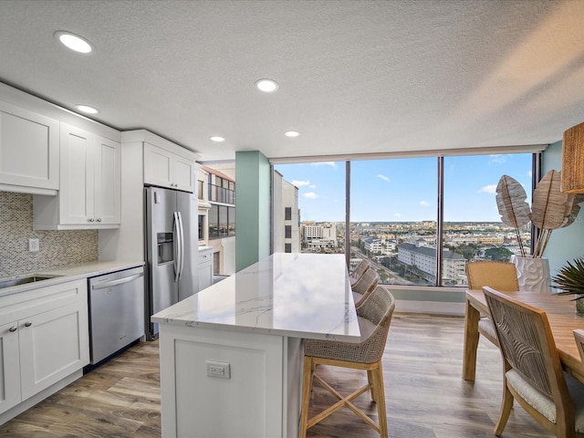 kitchen with appliances with stainless steel finishes, white cabinetry, a kitchen island, and light stone countertops