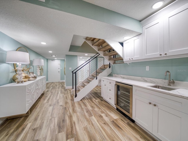 bar featuring light stone countertops, beverage cooler, white cabinetry, light hardwood / wood-style floors, and sink