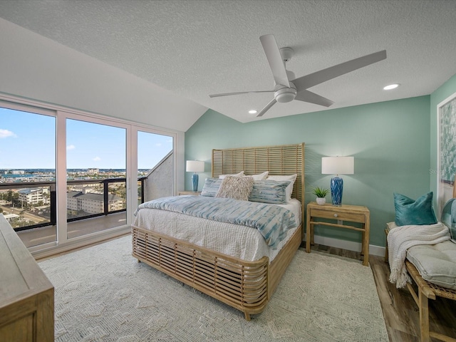 bedroom featuring ceiling fan, access to exterior, vaulted ceiling, hardwood / wood-style flooring, and a textured ceiling