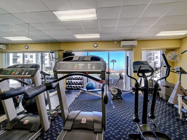 exercise room featuring a paneled ceiling, plenty of natural light, and a wall mounted air conditioner