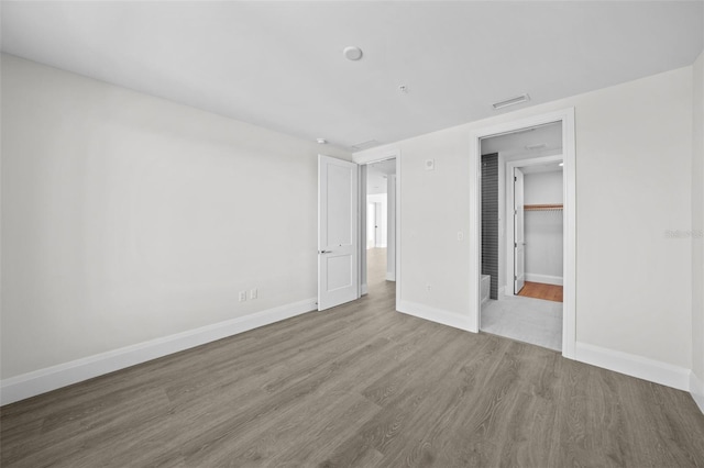 unfurnished bedroom featuring a spacious closet, wood-type flooring, and a closet