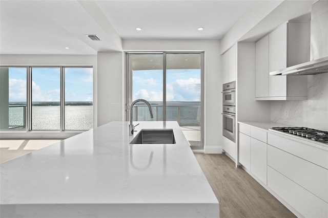 kitchen with white cabinets, wall chimney exhaust hood, tasteful backsplash, sink, and a water view