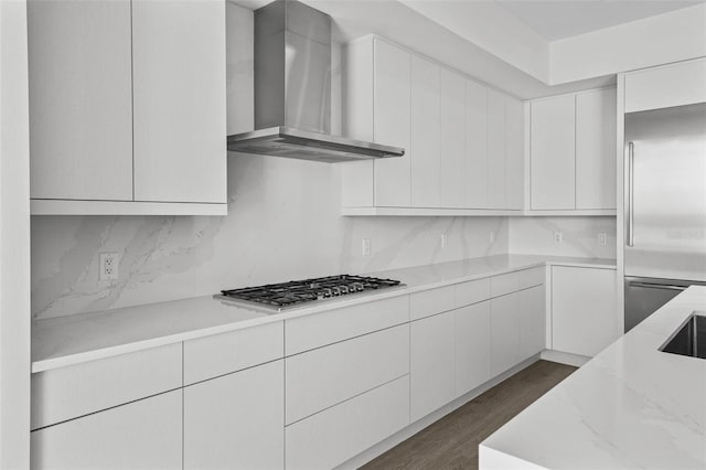 kitchen with wall chimney range hood, light stone counters, stainless steel appliances, and white cabinetry