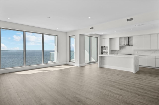 unfurnished living room with a water view, plenty of natural light, sink, and light hardwood / wood-style flooring