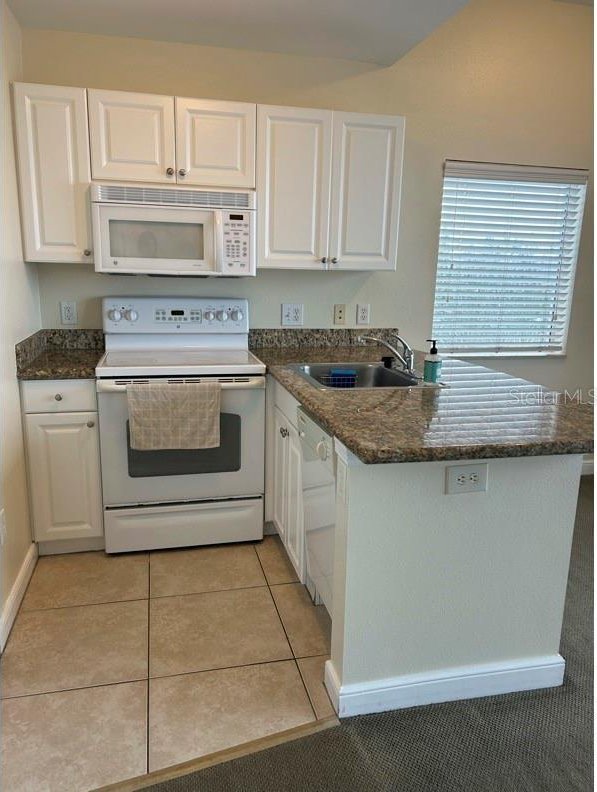 kitchen with white cabinetry, sink, white appliances, and light tile patterned flooring