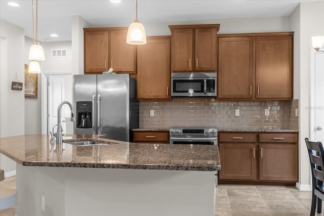 kitchen featuring pendant lighting, tasteful backsplash, dark stone countertops, a center island with sink, and stainless steel appliances