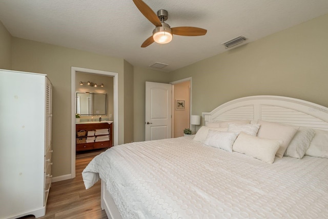 bedroom featuring light wood-type flooring, connected bathroom, a textured ceiling, and ceiling fan