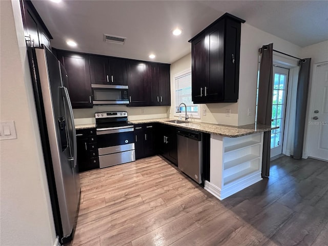 kitchen featuring appliances with stainless steel finishes, sink, light stone counters, and light hardwood / wood-style flooring