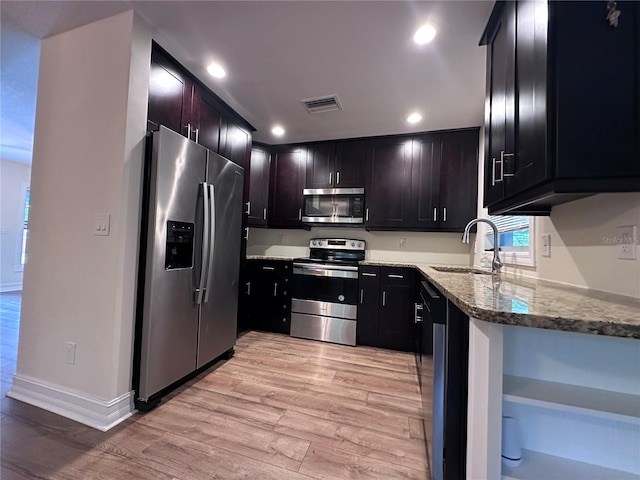 kitchen with sink, light wood-type flooring, light stone countertops, and appliances with stainless steel finishes